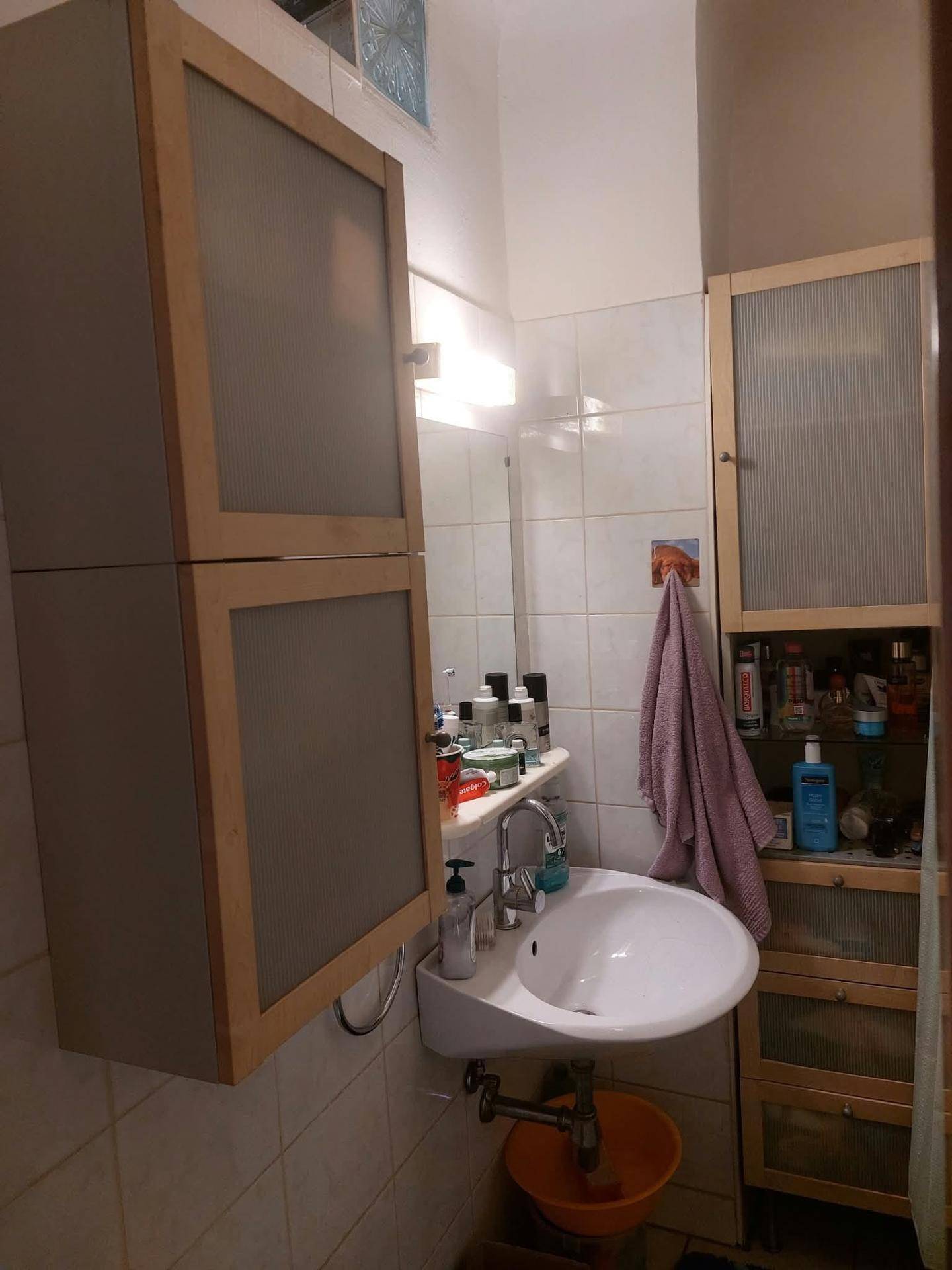 Kleines Badezimmer mit Waschbecken, Spiegelschrank und hellen Fliesen an den Wänden.