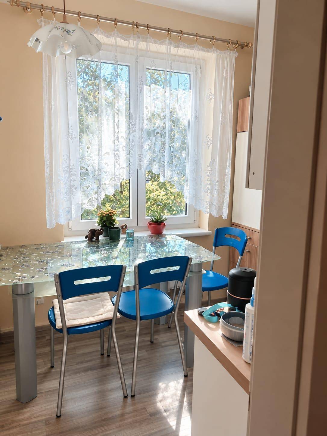 Essbereich in der Küche mit Glastisch, blauen Stühlen und viel Tageslicht durch das Fenster.