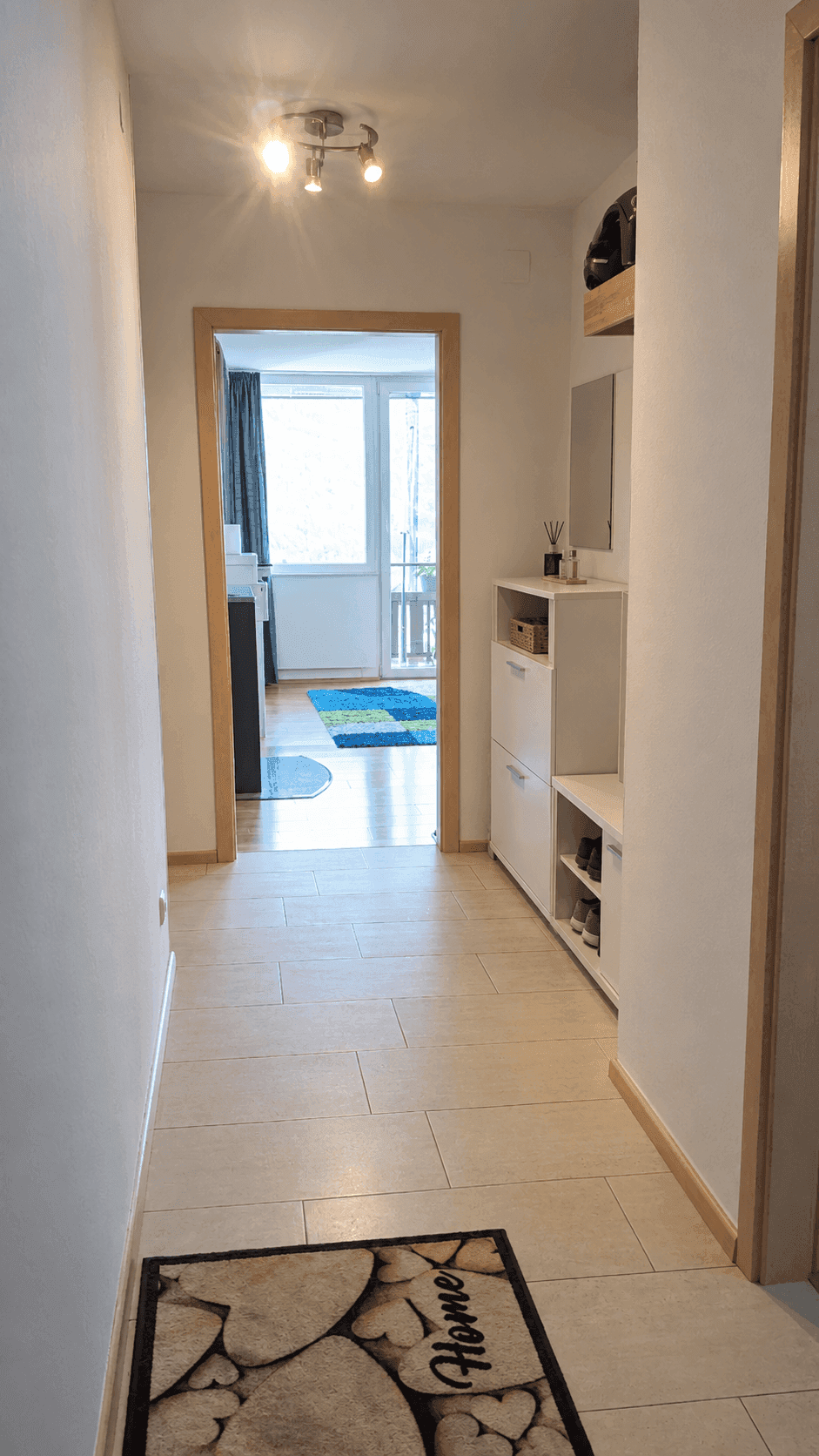 Heller Flur mit Fliesenboden, modernem Schuhschrank und Zugang zu einem Balkon.