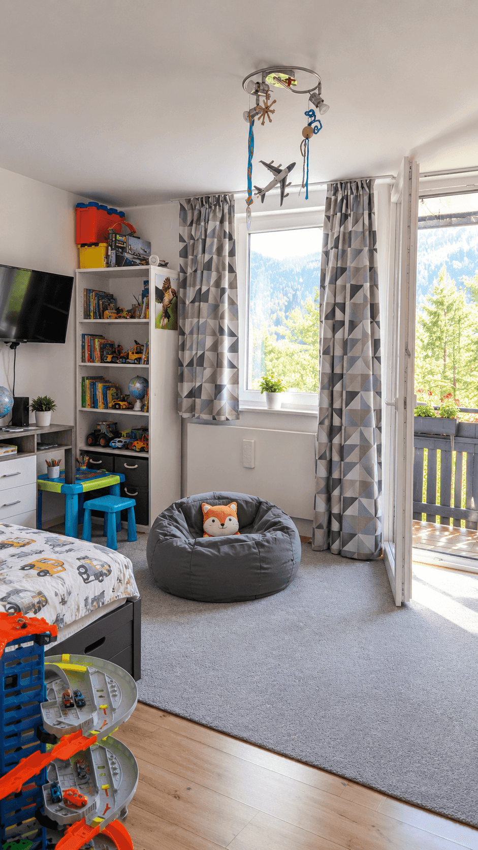 Kinderzimmer mit Spielzeug, Teppichboden und Zugang zu einem kleinen Balkon mit Bergblick.