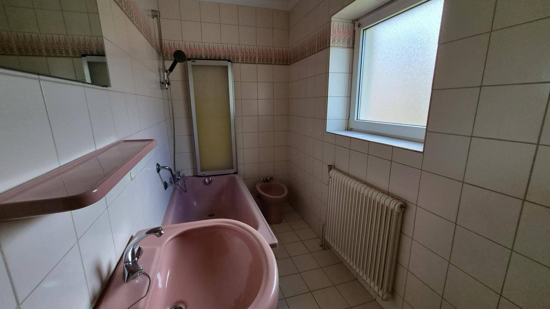 Badezimmer im Stil der 80er Jahre mit rosa Badewanne, Waschbecken und weißen Fliesen.