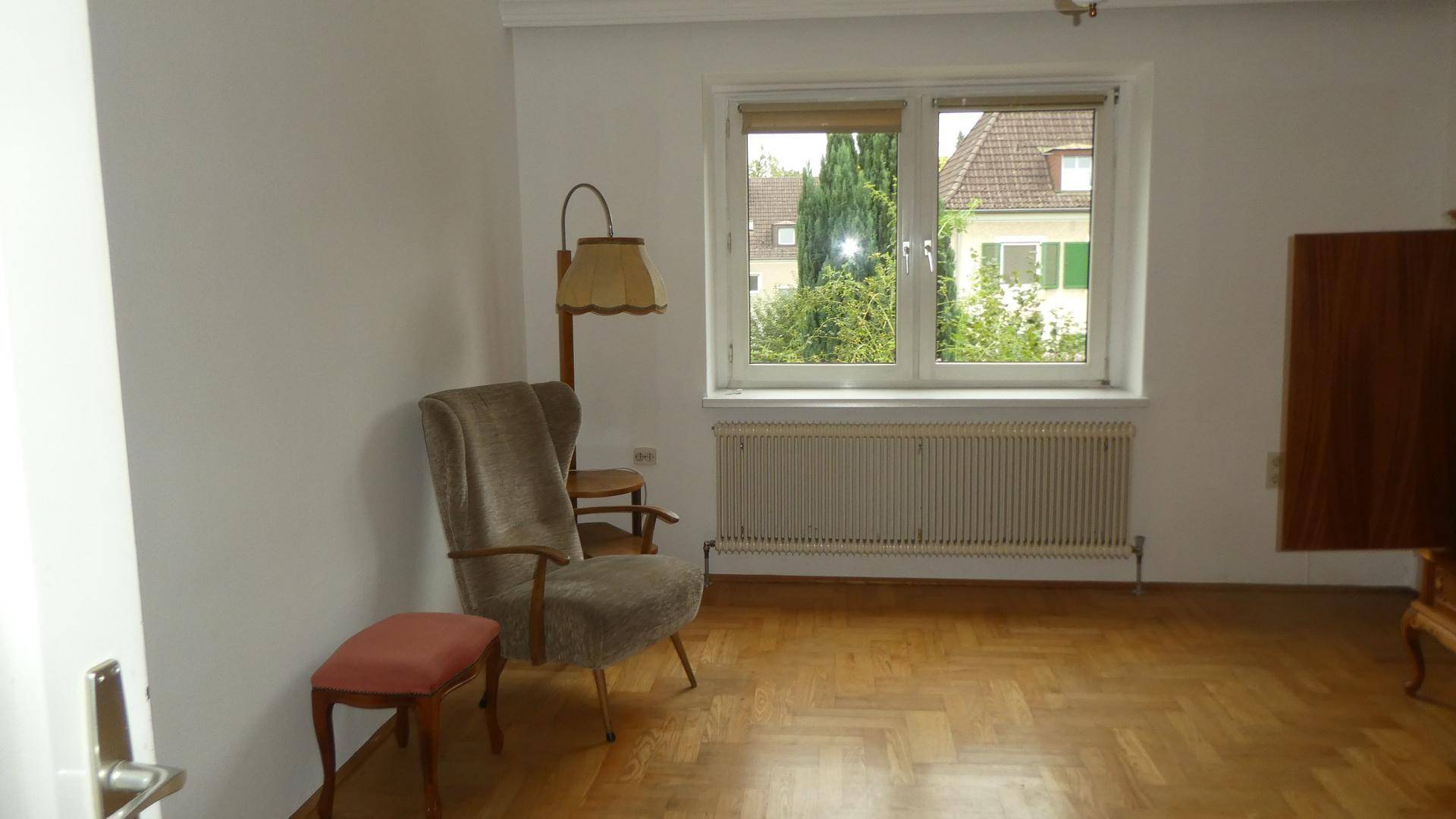 Gemütlicher Raum mit Parkettboden, Sessel und Blick ins Grüne durch das Fenster.
