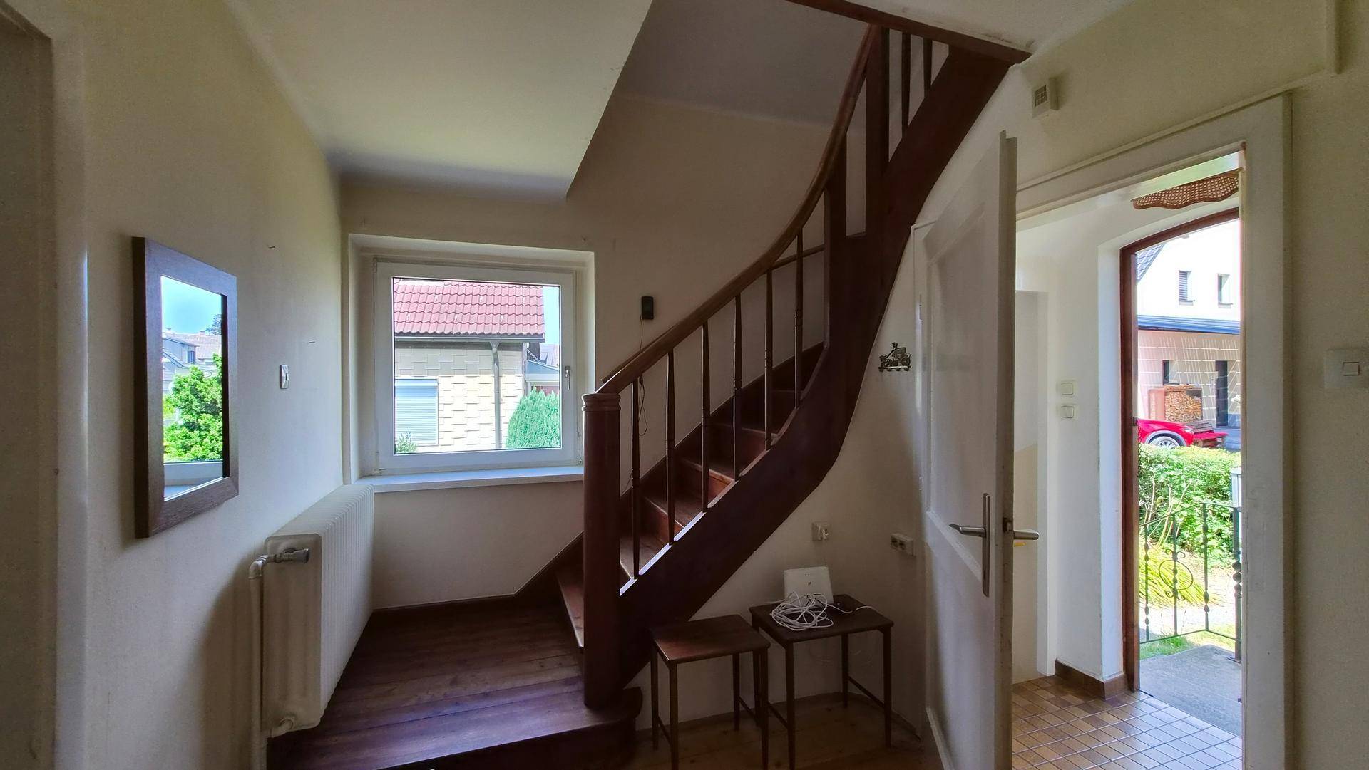 Eingangsbereich mit Holztreppe, Fenster und Zugang zum Obergeschoss.