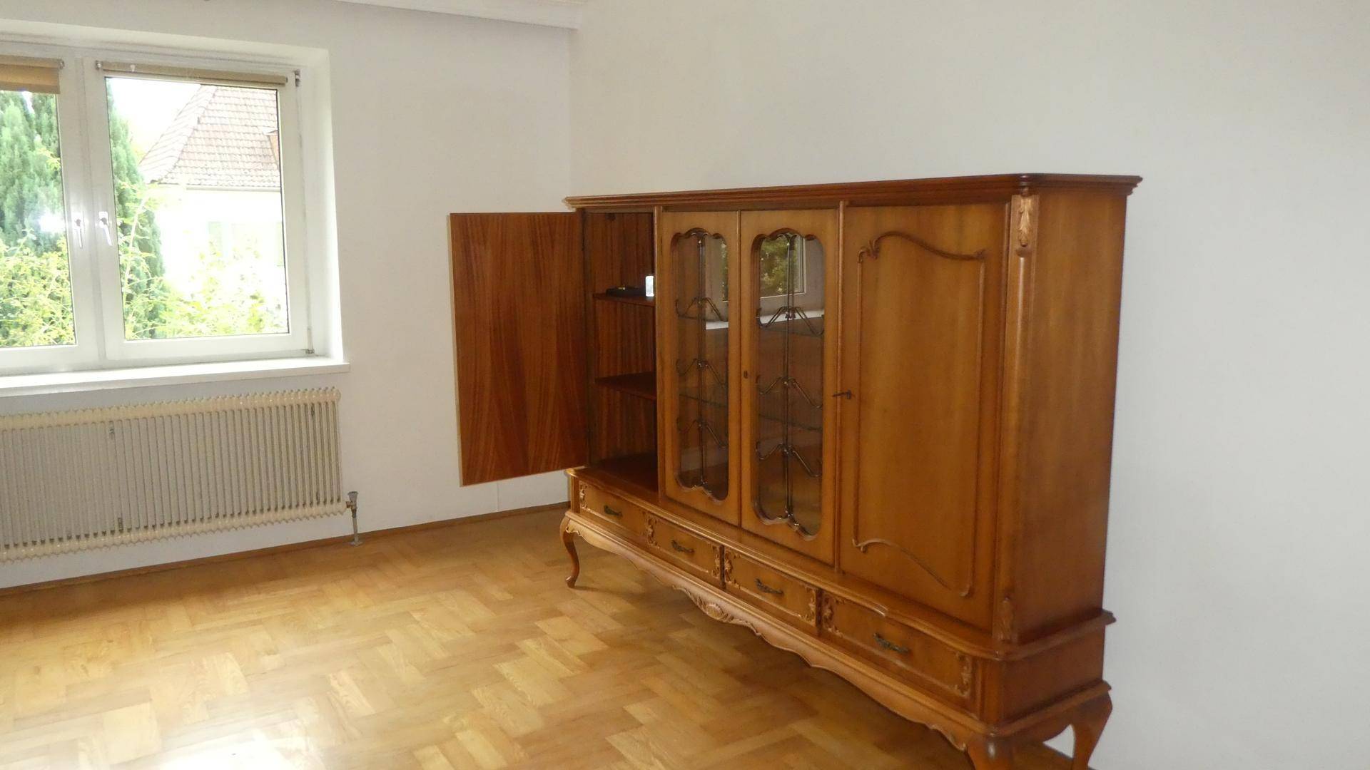 Wohnbereich mit Parkettboden und einem großen, traditionellen Holzschrank.