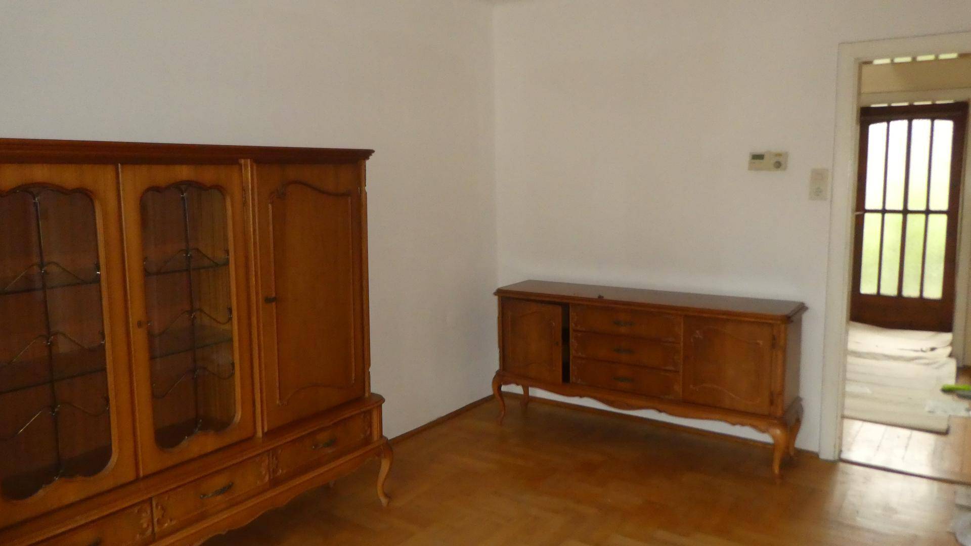 Wohnzimmer mit klassischem Holzschrank und Zugang zu einem weiteren Raum.