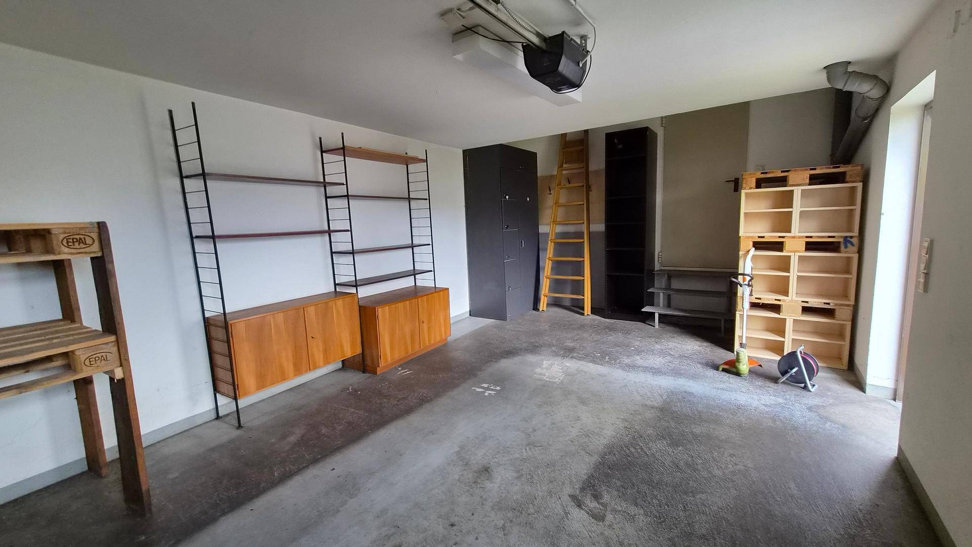 Geräumige Garage mit Betonboden und verschiedenen Regalsystemen für Lagerzwecke.