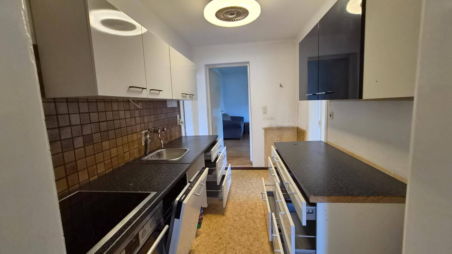 Funktionale Küche mit weißen Schränken, dunklen Arbeitsplatten und gefliestem Spritzschutz.