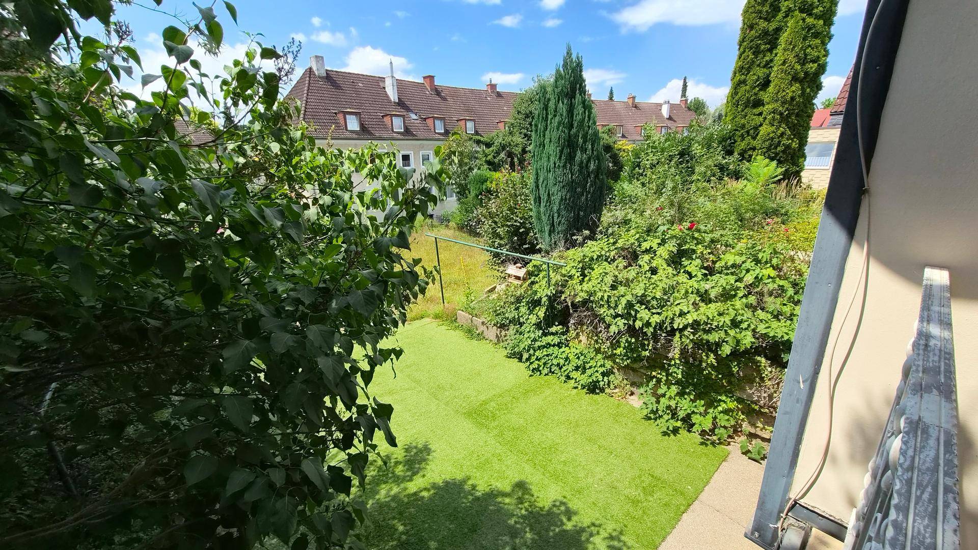 Blick vom Balkon auf den grünen Garten und die umliegende Wohnbebauung.