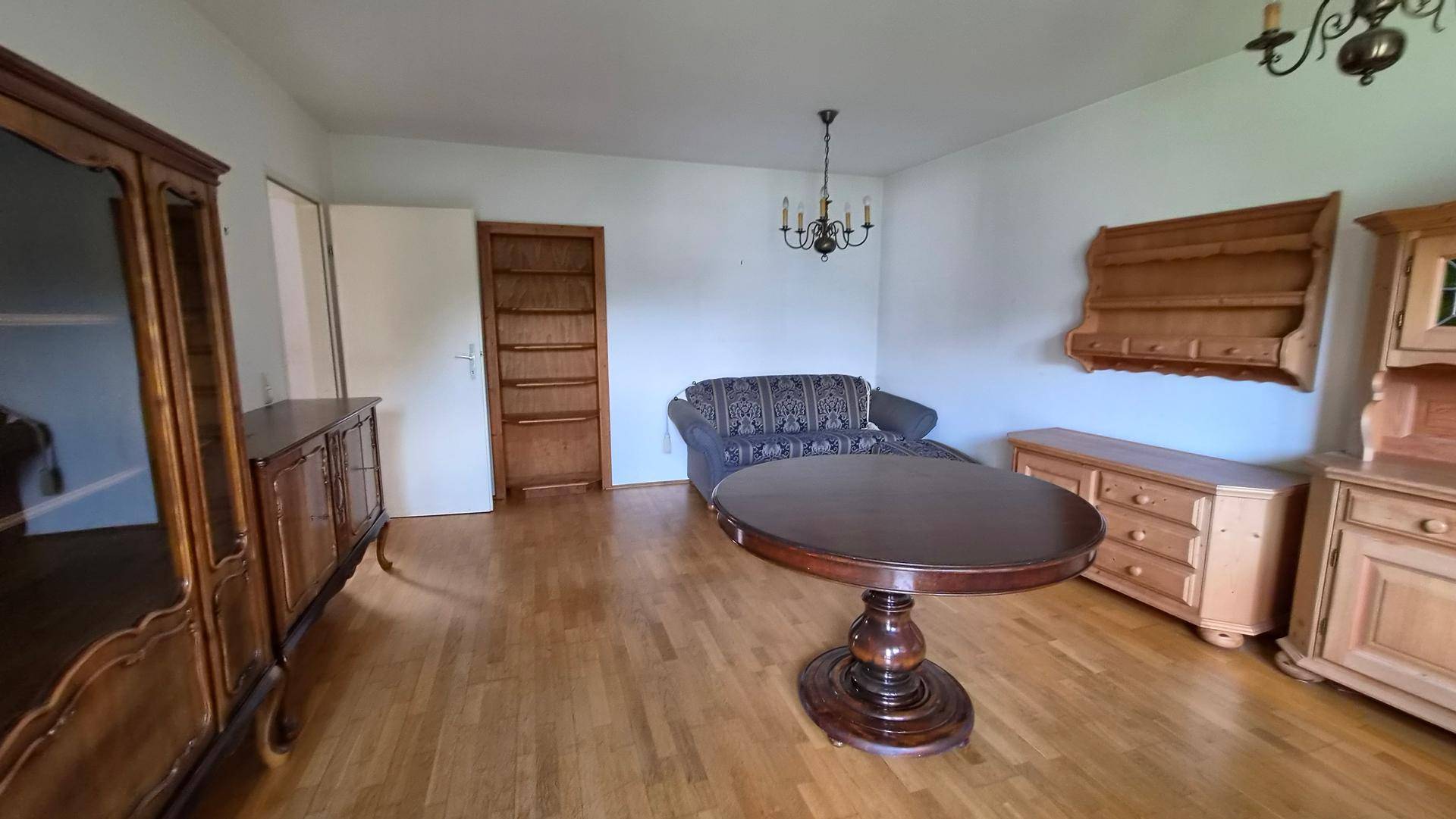 Geräumiges Wohnzimmer mit traditionellen Holzmöbeln, Parkettboden und Kronleuchter.