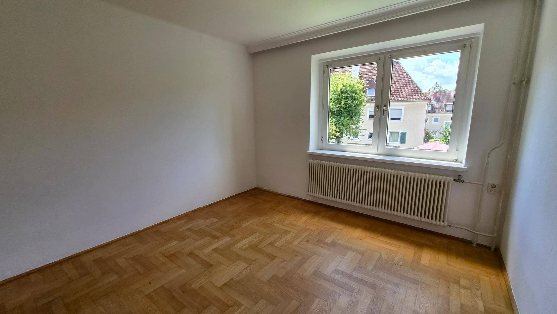 Geräumiger Raum mit Parkettboden und großem Fenster, das viel Tageslicht hereinlässt.