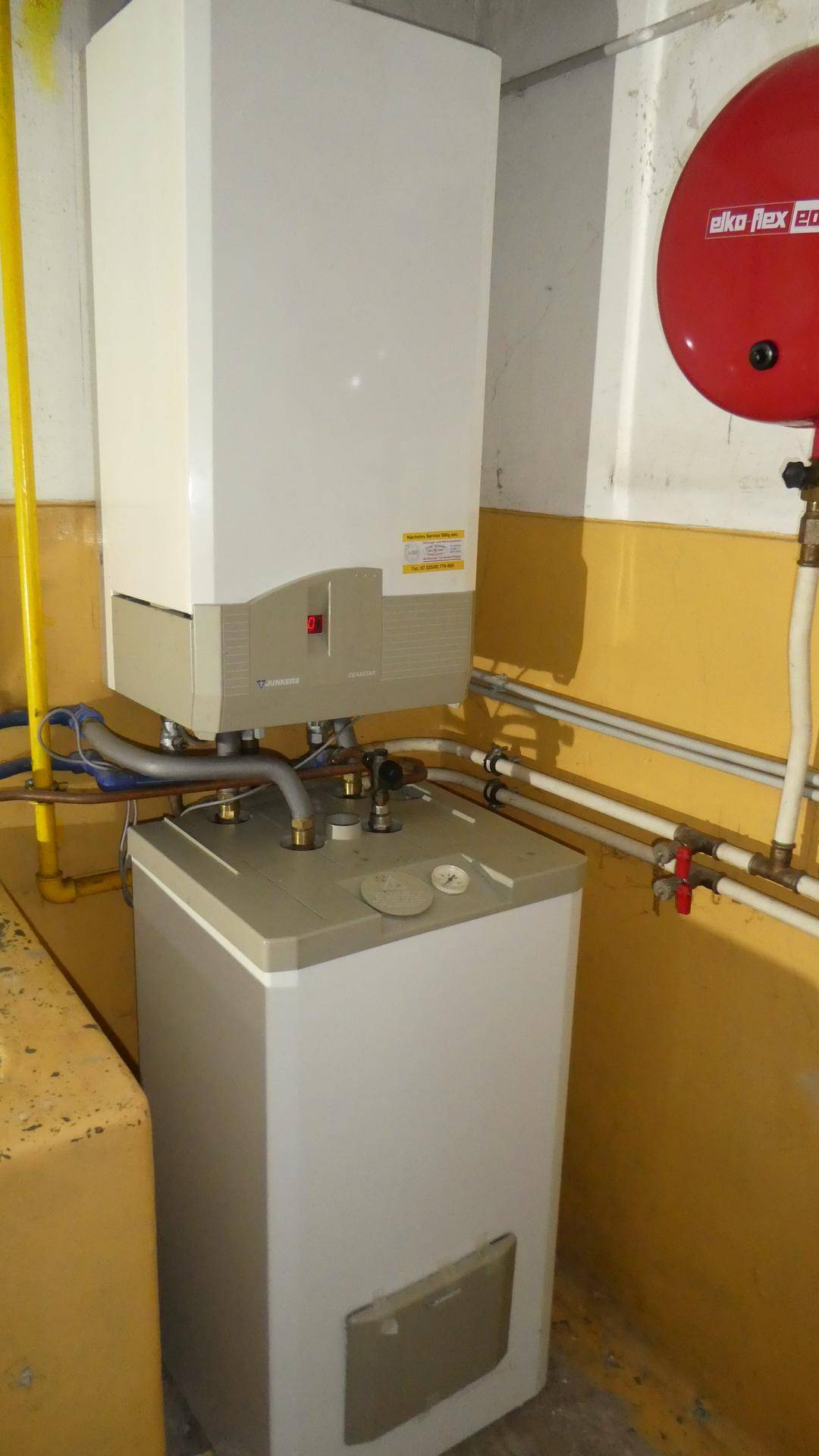 Heizungsanlage mit Warmwasserspeicher und sichtbaren Rohren in einem Technikraum.