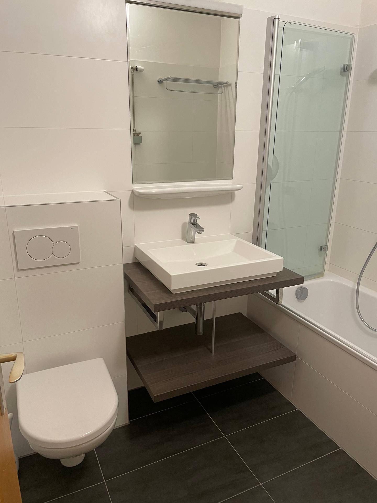 Modernes Badezimmer mit dunklen Bodenfliesen, Aufsatzwaschbecken und einer Dusch-Badewannen-Kombination.