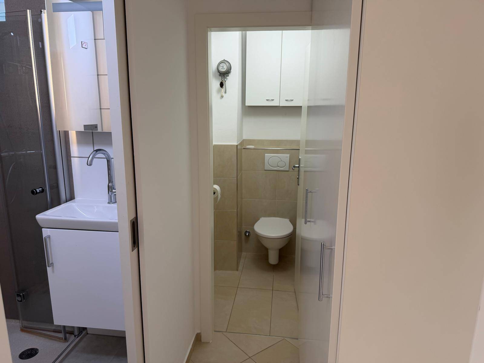 Modernes Badezimmer mit WC, Waschbecken und Duschbereich, hell gefliest und funktional.