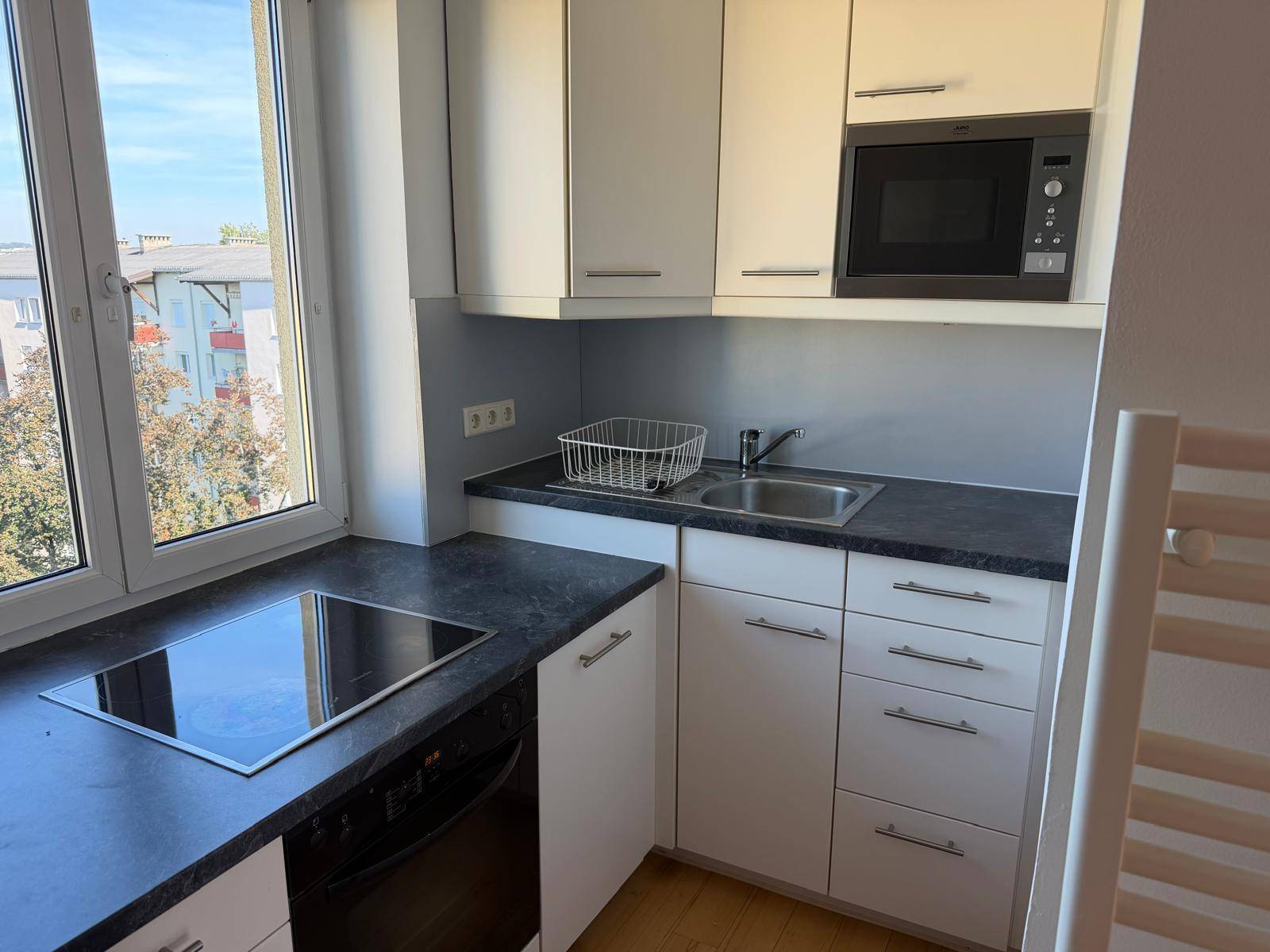Kleine, funktionale Küchenzeile mit Induktionskochfeld, Mikrowelle und Fenster mit Ausblick.