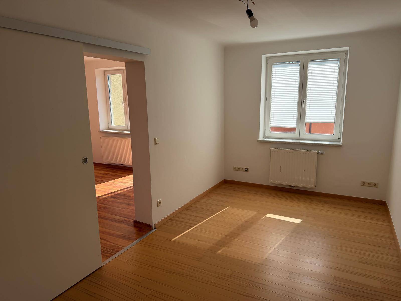 Geräumiges, helles Zimmer mit Holzboden und Schiebetür zu einem weiteren Raum, gut belichtet.