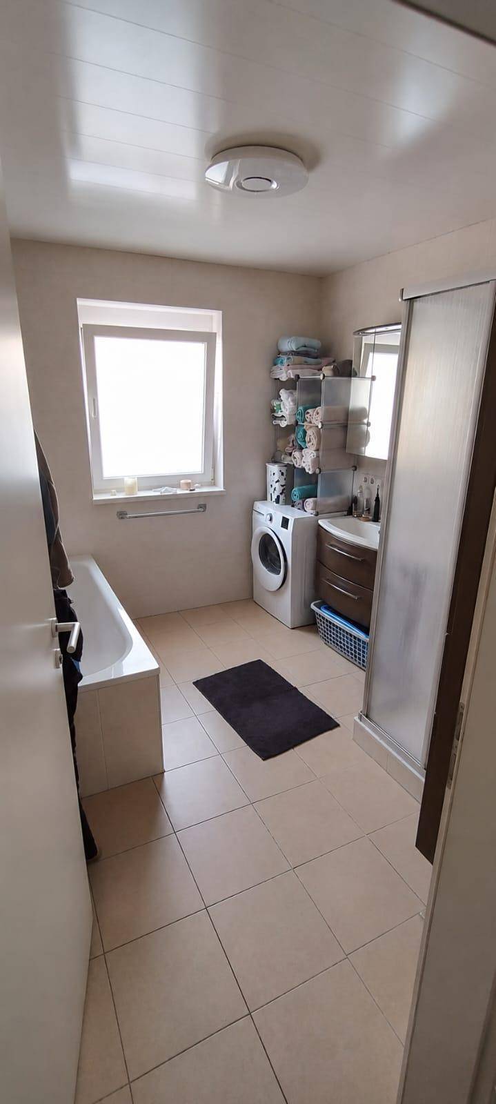 Badezimmer mit Badewanne, Dusche, Waschmaschine und Fenster.