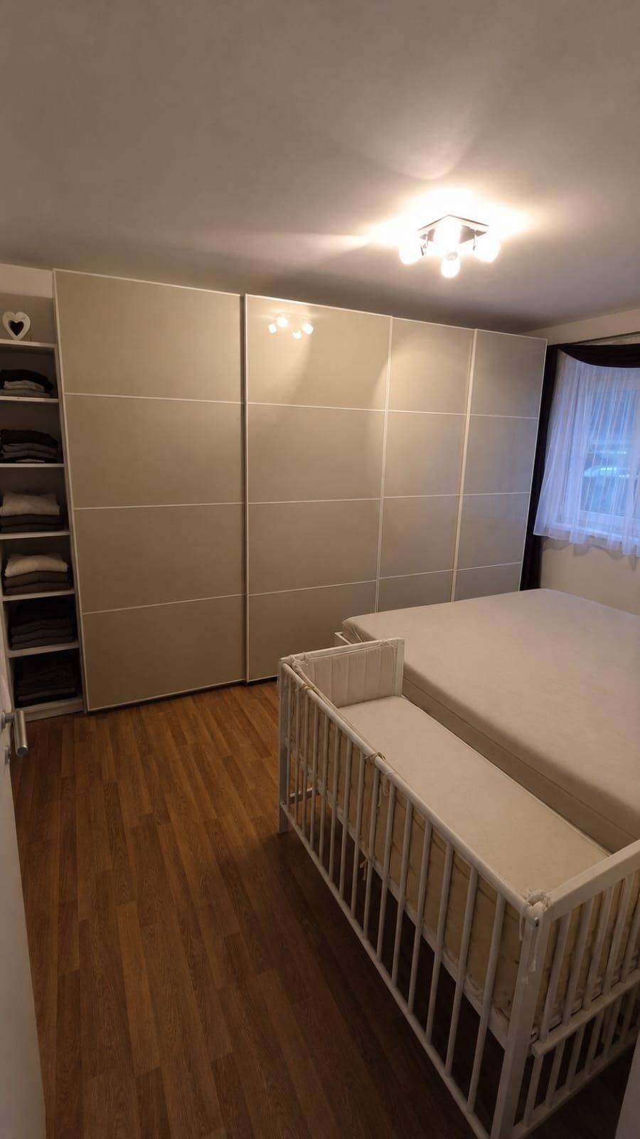 Schlafzimmer mit großem Kleiderschrank, Holzboden und Babybett.
