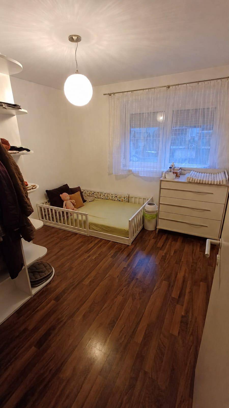 Kinderzimmer mit Holzboden, Fenster und praktischer Wickelkommode.