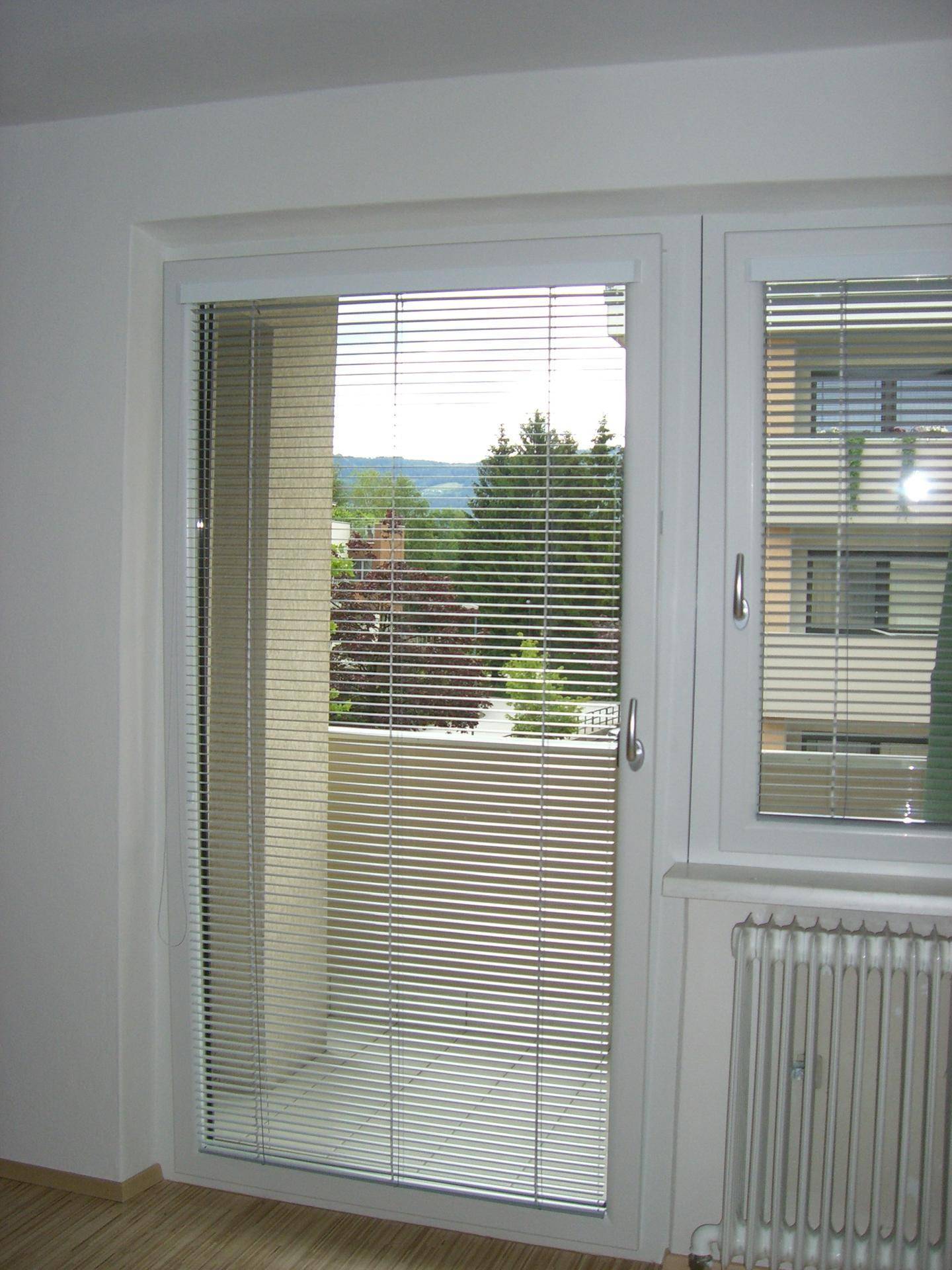 Fenster und Balkontür mit Jalousien, die einen Blick ins Grüne ermöglichen.