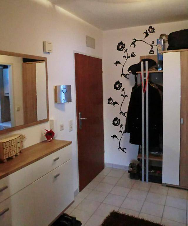 Eingangsbereich mit Fliesenboden, Spiegel, Kommode und Garderobe an der Wand.