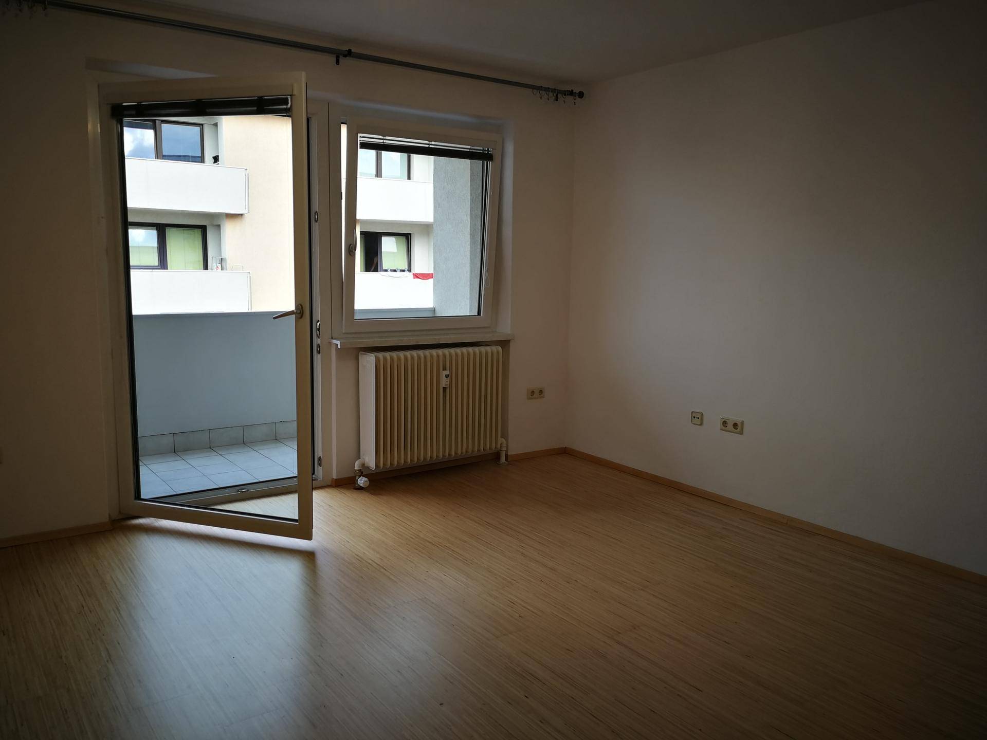 Leerer Raum mit Laminatboden, Heizkörper und Zugang zu einem kleinen Balkon.