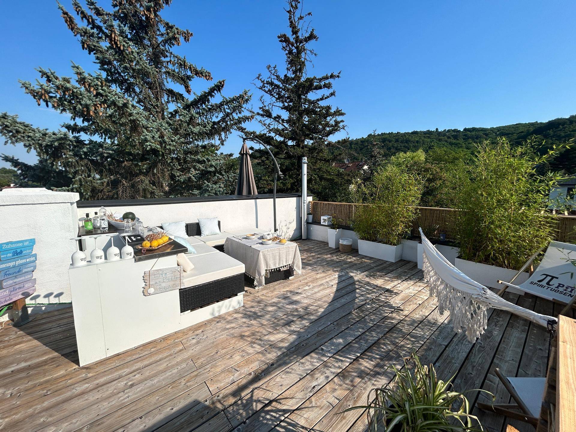 Geräumige Dachterrasse mit Holzbelag, bequemen Loungemöbeln und üppiger Bepflanzung unter blauem Himmel.