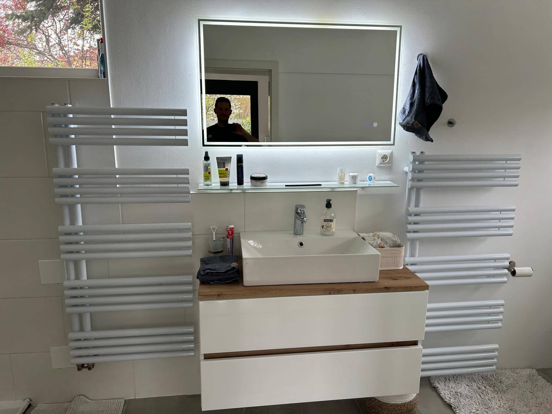 Modernes Badezimmer mit Einzelwaschbecken, beleuchtetem Spiegel und zwei beheizten Handtuchhaltern.
