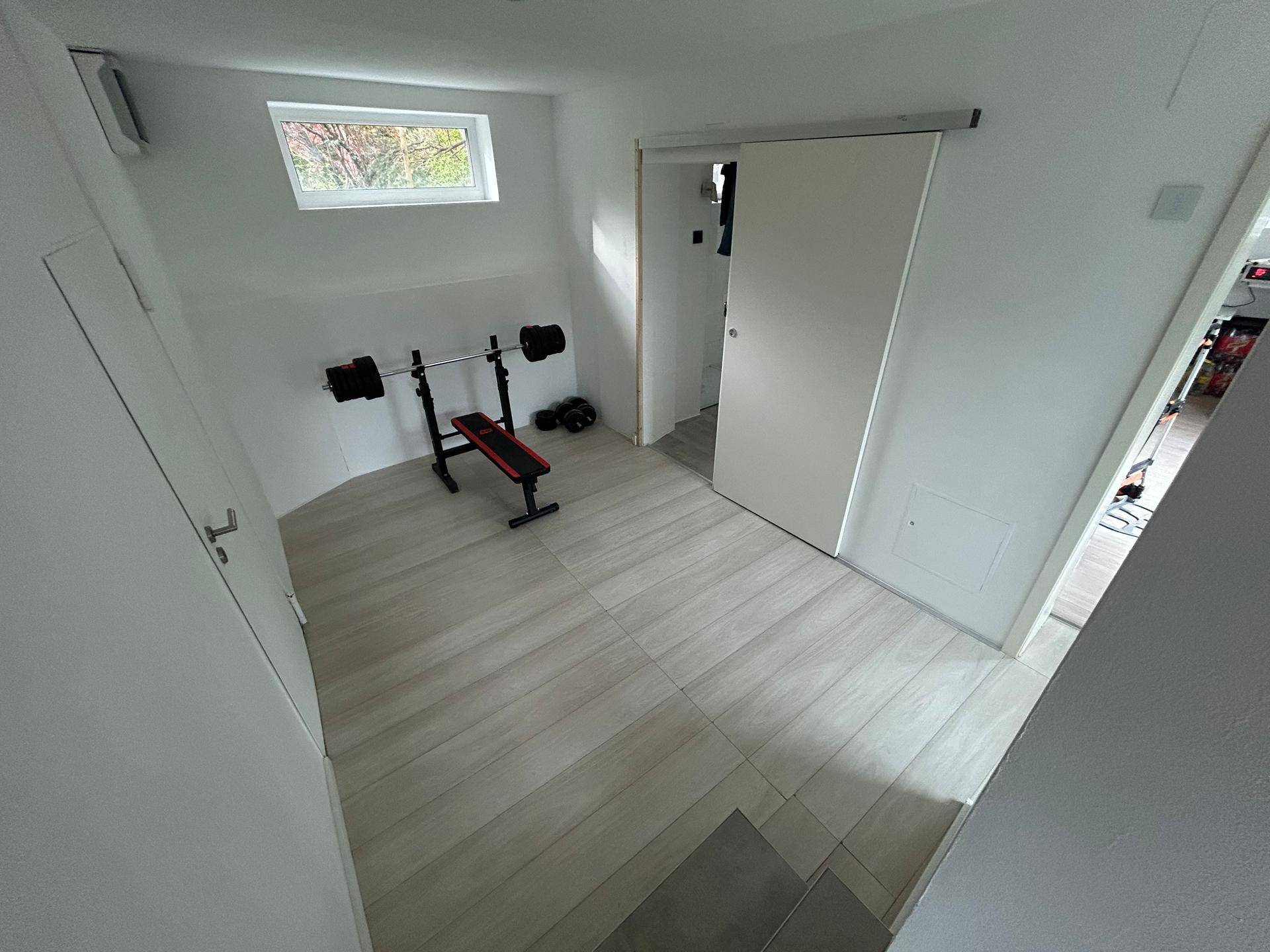 Kleiner Fitnessraum mit Hantelbank und Gewichten, ausgestattet mit einem Dachfenster für natürliches Licht.