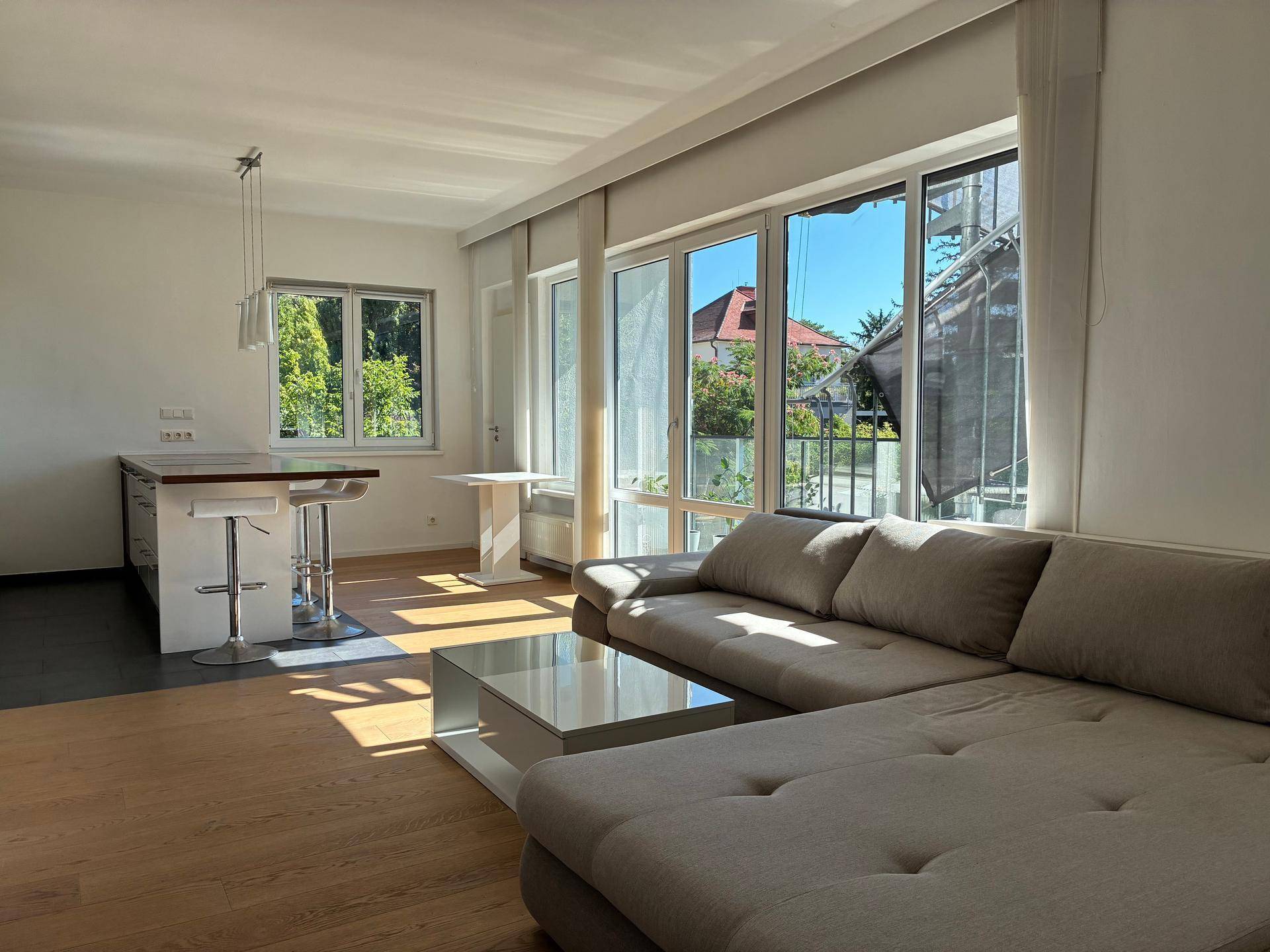Heller offener Wohnbereich mit großem Sofa, Holzboden und integrierter Küchenzeile mit Barhockern.