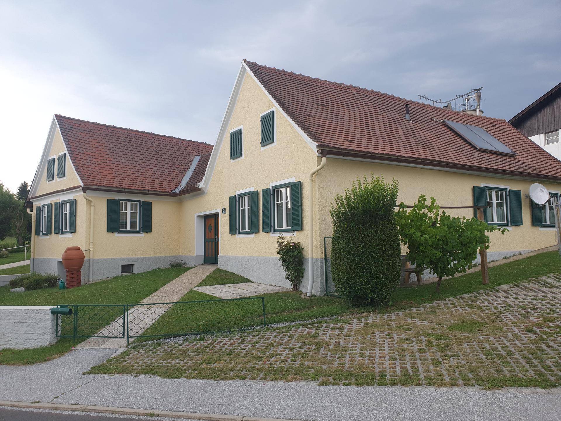 Traditionelles Einfamilienhaus mit gelber Fassade, grünen Fensterläden und Satteldach in ländlicher Umgebung.