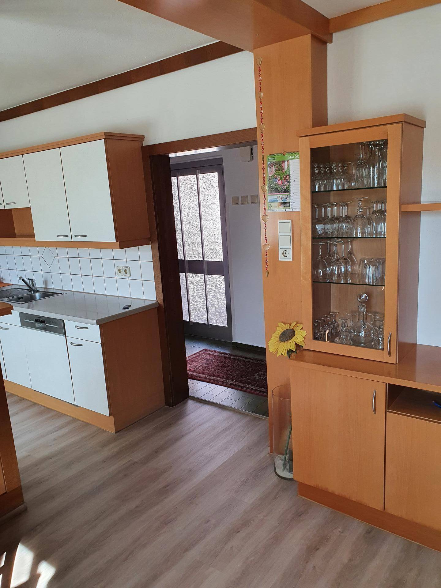 Teilansicht einer Küche mit hellen Schränken, Fliesenrückwand und Durchgang zum Flur.