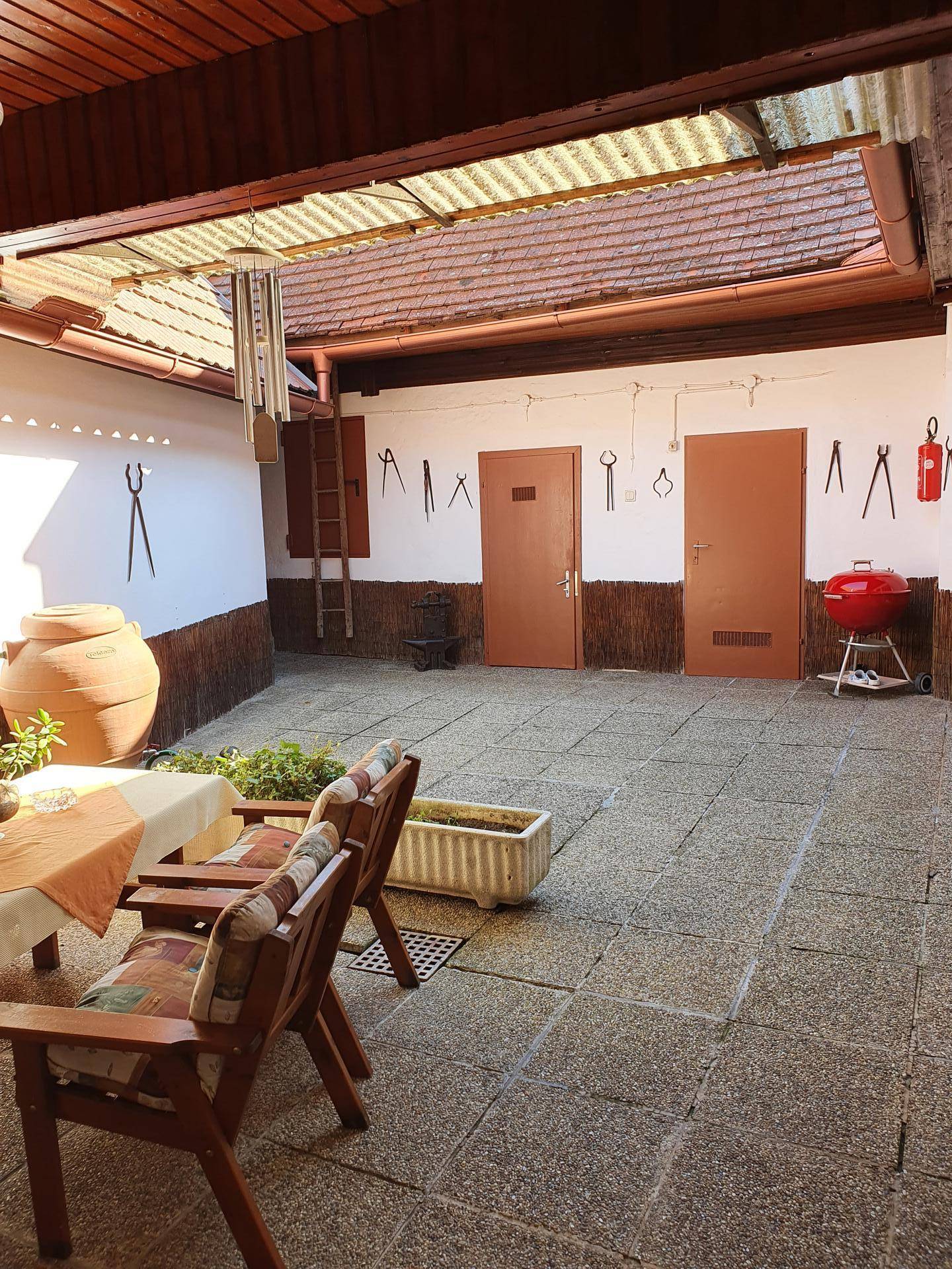 Geräumiger überdachter Innenhof mit Steinfliesen, Grill und dekorativen Werkzeugen an der Wand.