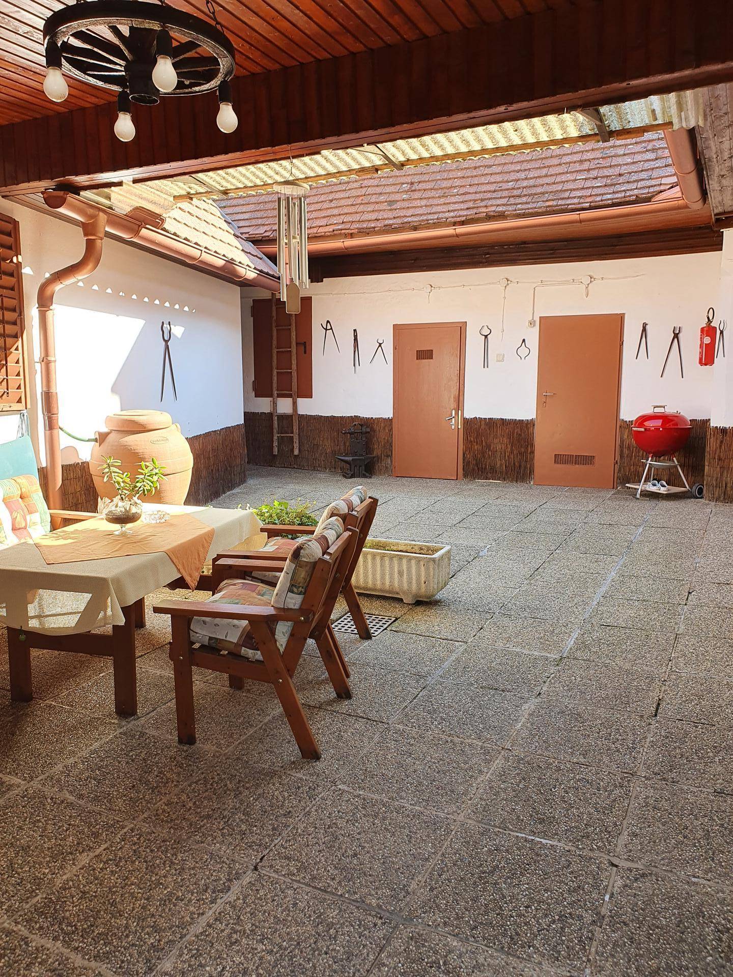 Überdachter Innenhof mit Sitzgelegenheiten, Steinfliesen und einem roten Grill.