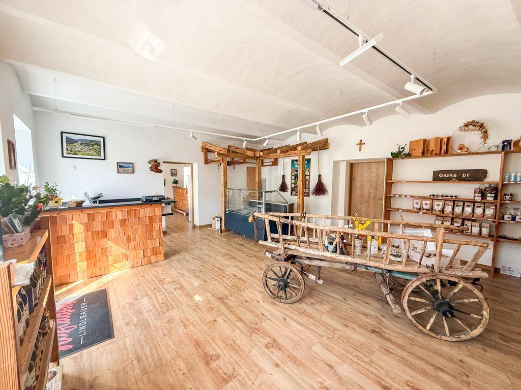 Einladender Verkaufsraum mit rustikalem Holzwagen, Regalen und Blick in angrenzende Bereiche.