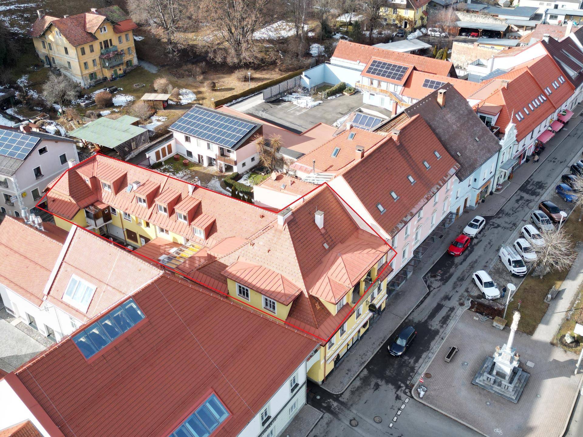 Weitläufige Luftaufnahme einer Stadtstraße mit mehreren Gebäuden, roten Ziegeldächern und einigen Solaranlagen.