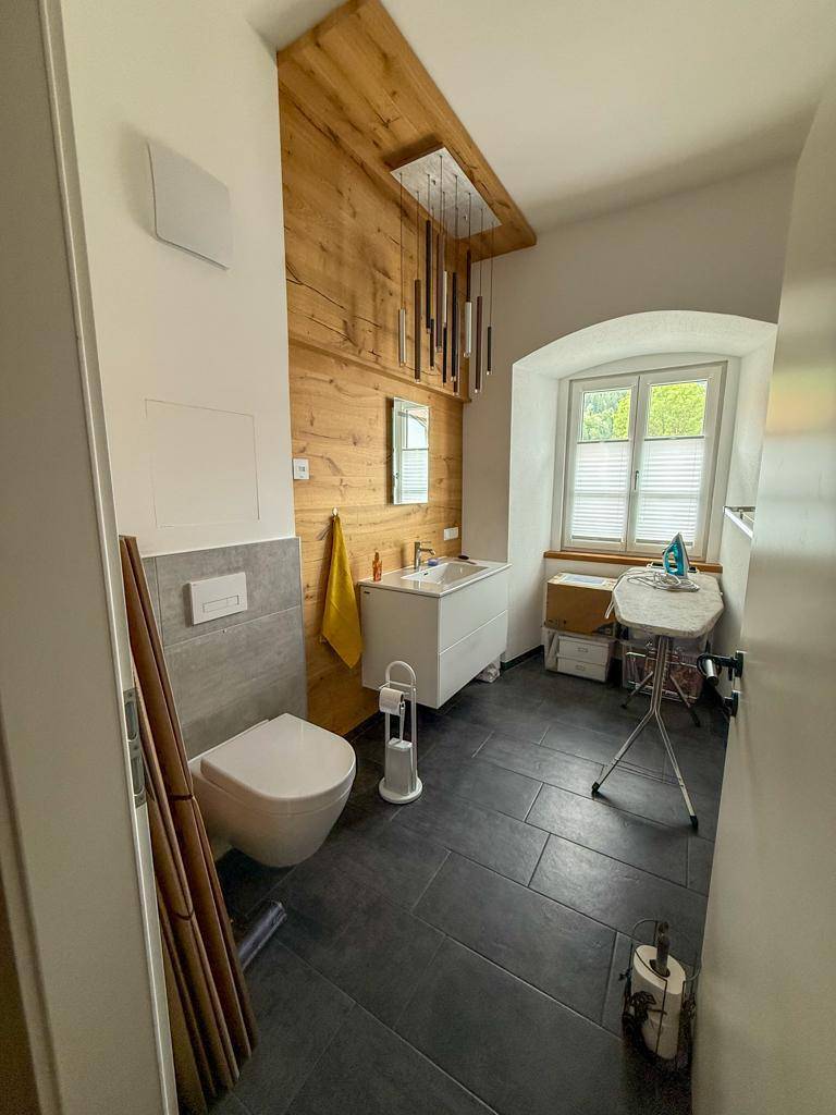 Modernes WC mit Holzverkleidung, Wand-WC, Waschbecken und Fenster.