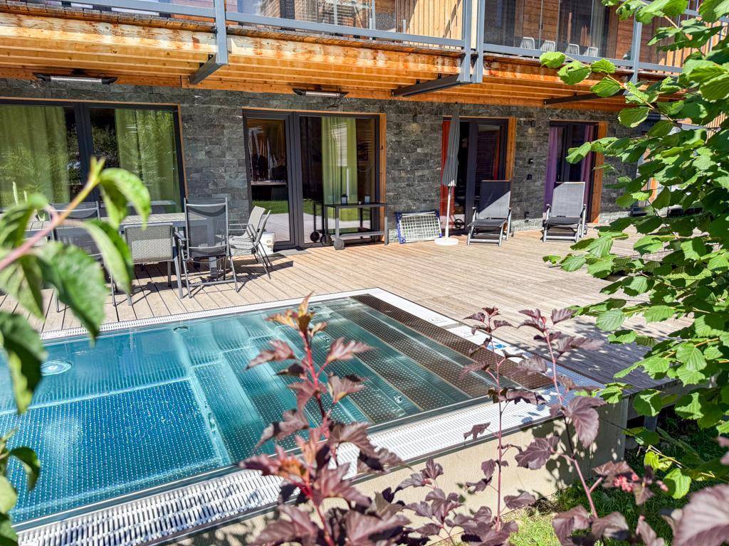 Geräumige Holzterrasse mit Pool, Liegestühlen und Zugang zu den Wohnbereichen des Gebäudes.