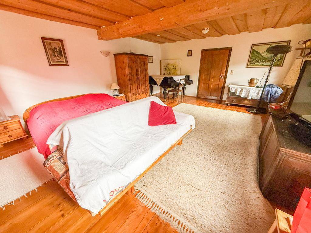 Schlafzimmer mit Holzboden, freiliegenden Deckenbalken und einem Klavier, hell und geräumig gestaltet.