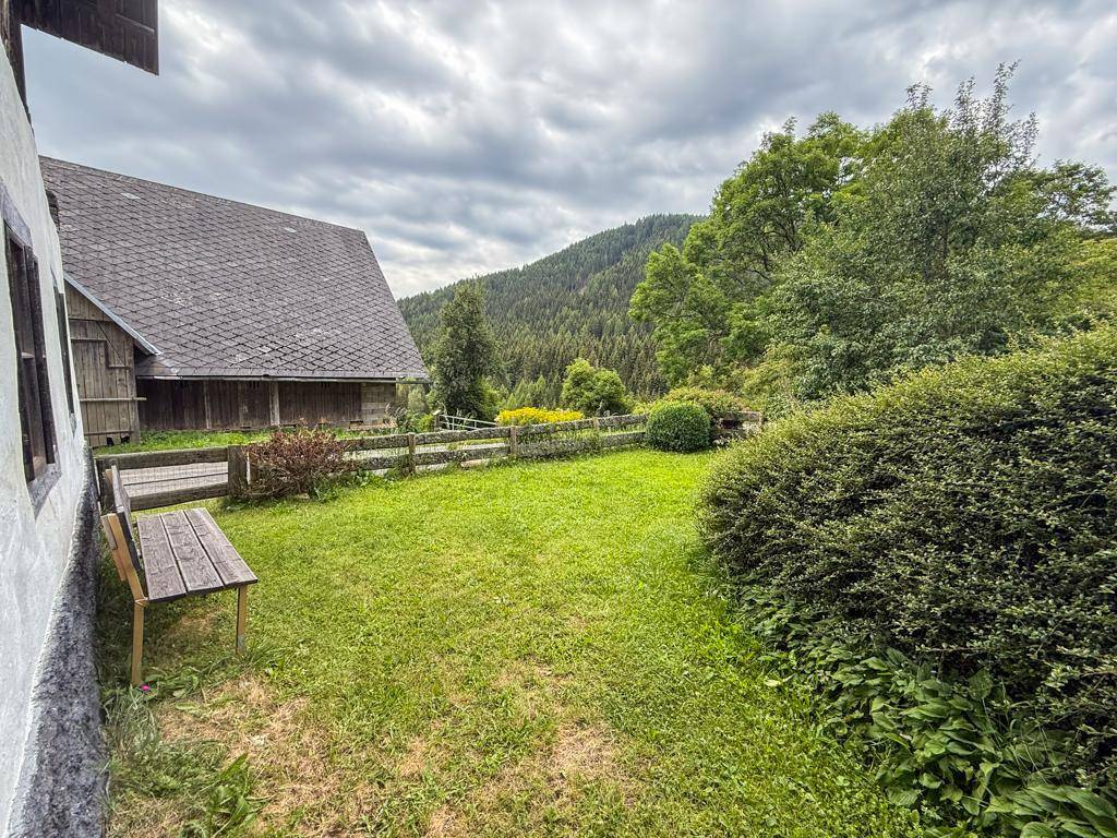 Gepflegter Gartenbereich mit Rasenfläche, Büschen und einem Holzzaun, umgeben von Natur und Bäumen.