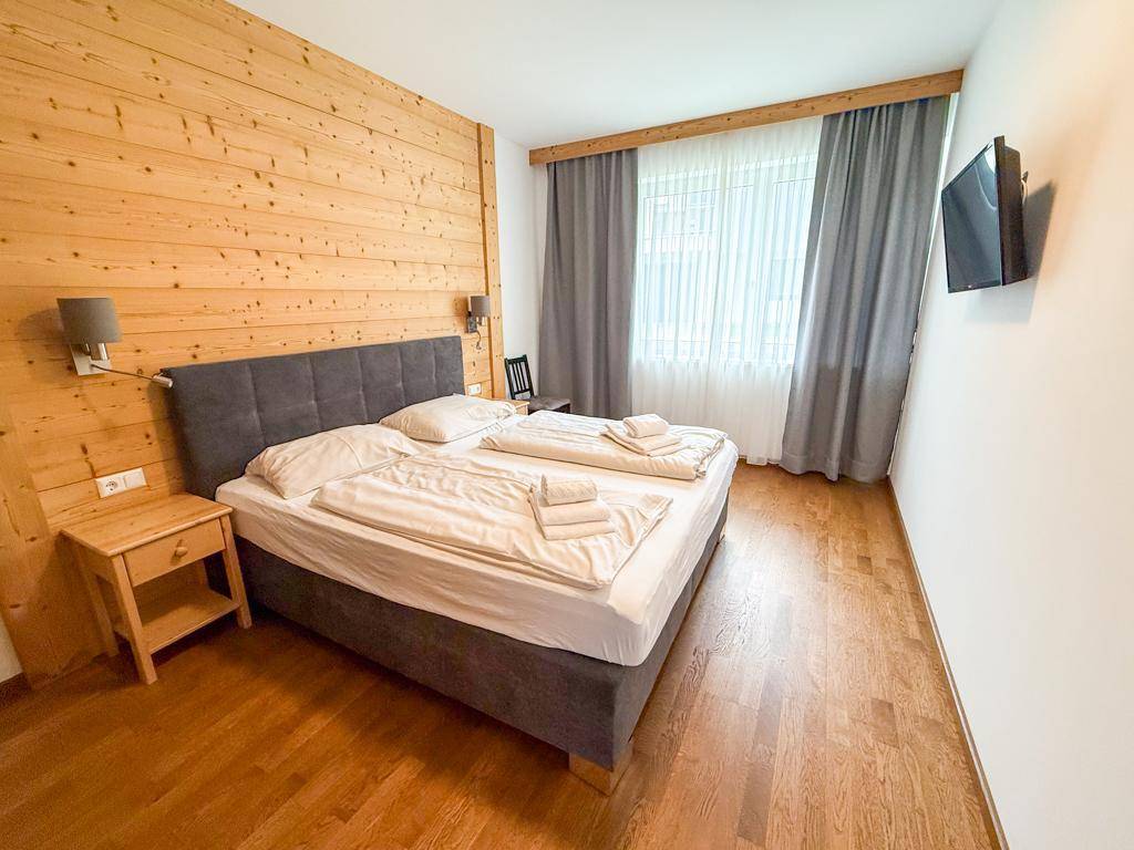 Helles Schlafzimmer mit Doppelbett, Holzwand und Fernseher an der Wand.