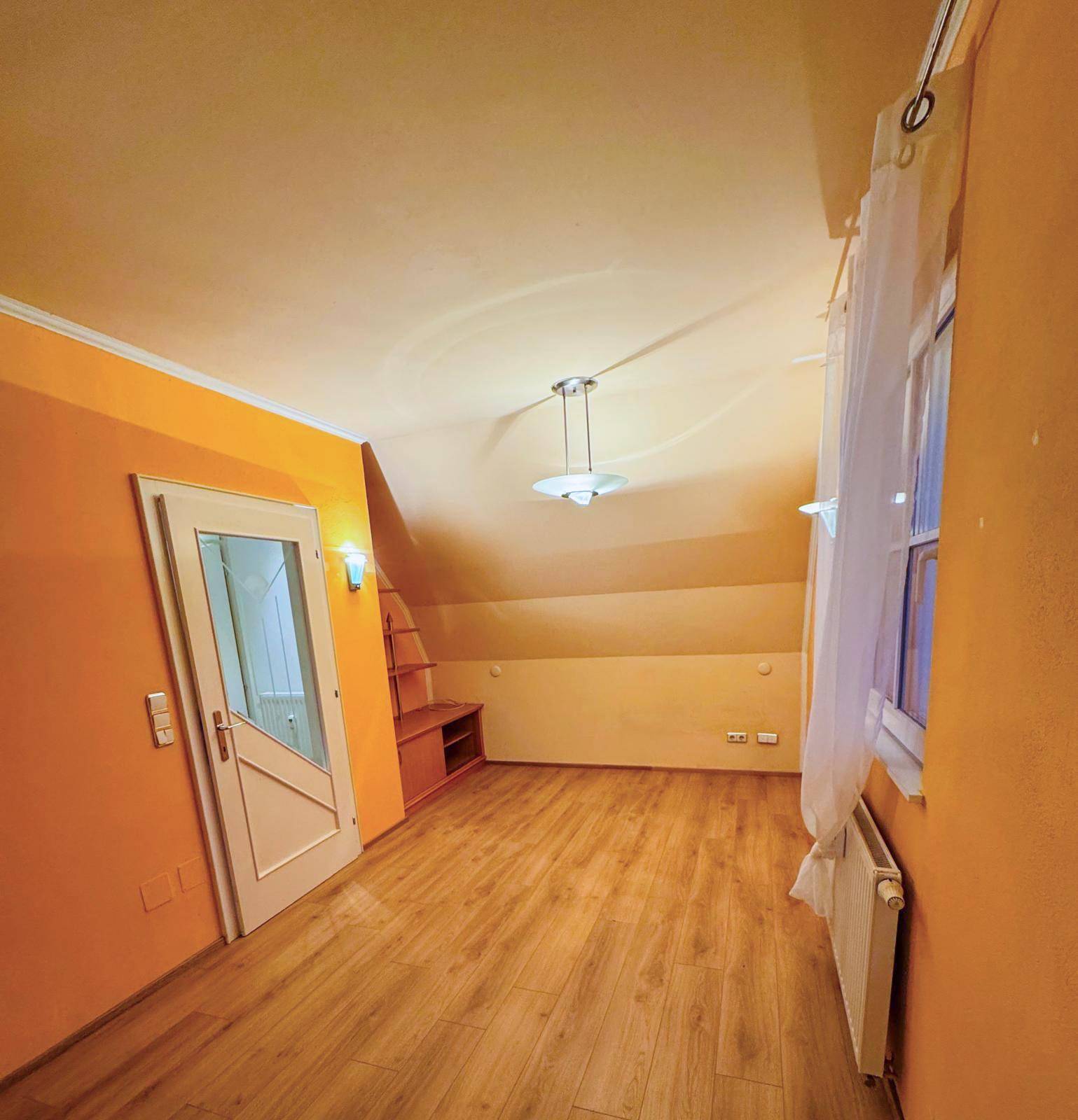 Heller Wohnraum mit Dachschräge, Laminatboden und orangefarbenen Wänden.