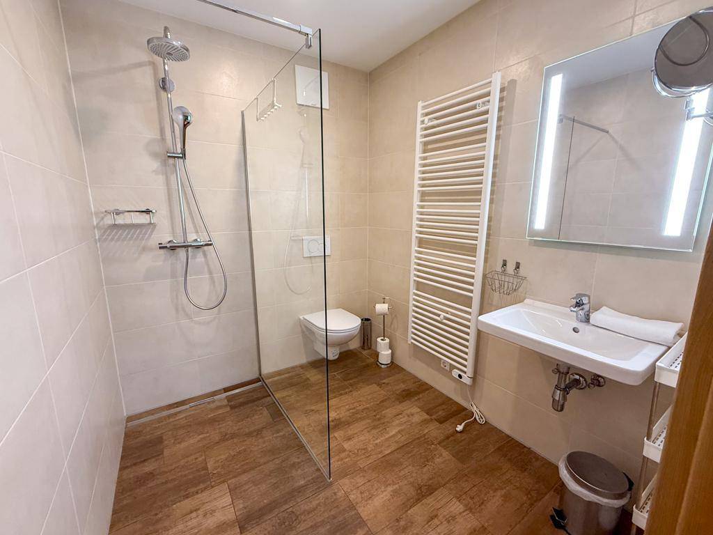 Helles Badezimmer mit ebenerdiger Dusche, WC und beheiztem Handtuchhalter.