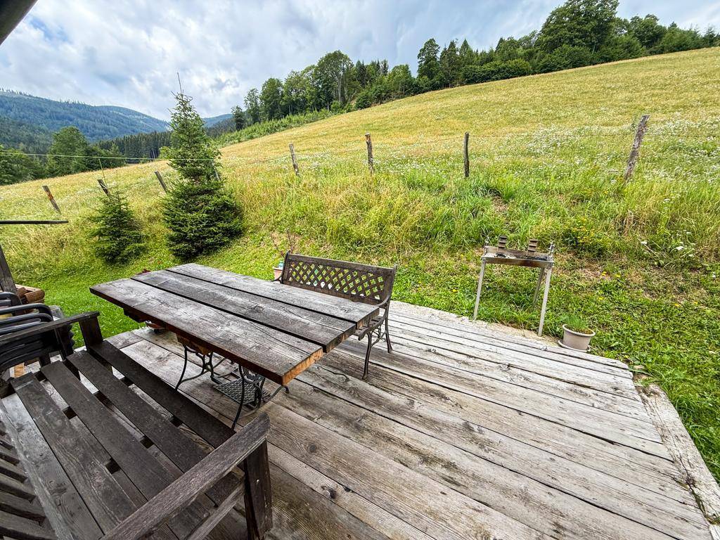 Rustikale Holzterrasse mit Sitzgelegenheiten und Blick auf die umliegende grüne Landschaft und Hügel.