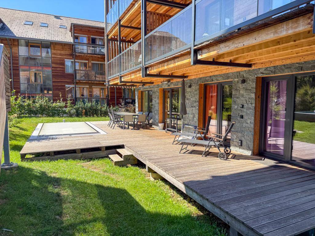 Weitläufige Holzterrasse mit Rasenfläche, Pool und Balkonen an der modernen Gebäudefassade.