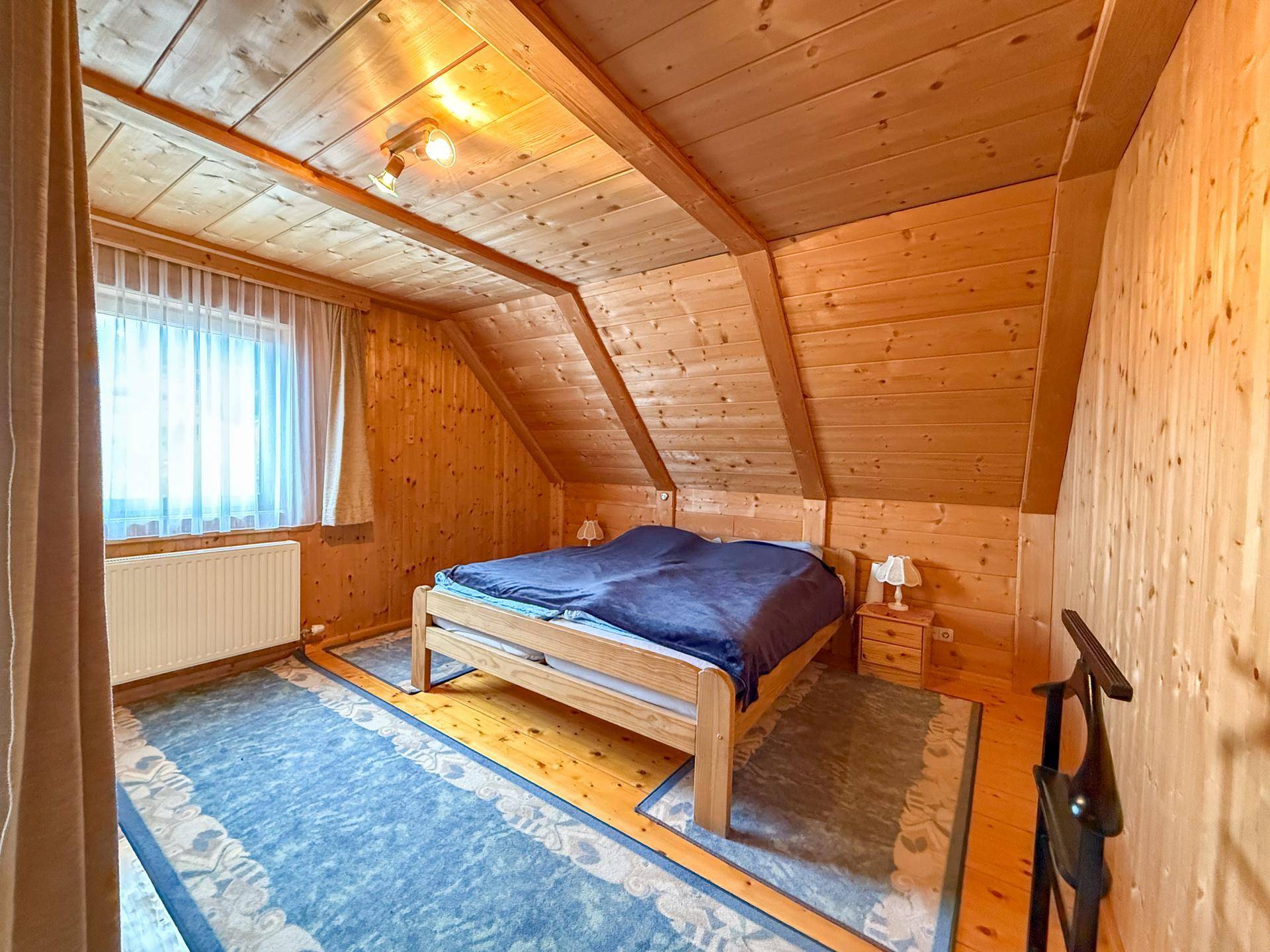 Gemütliches Schlafzimmer im Dachgeschoss mit Holztäfelung, Holzboden und einem Fenster.
