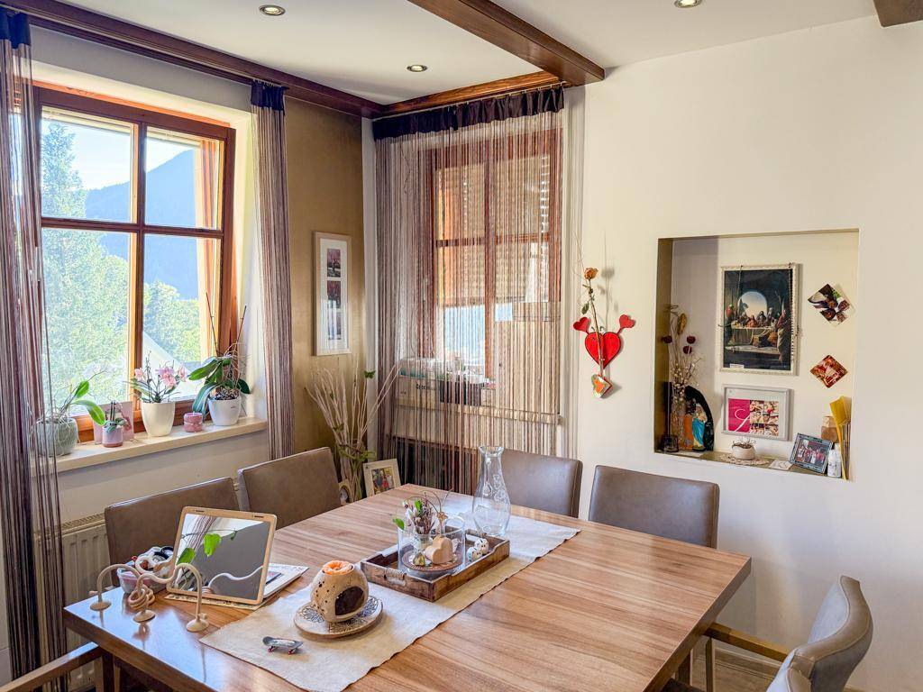 Heller Essbereich mit Holztisch, gemütlichen Stühlen und Bergblick durch die Fenster.