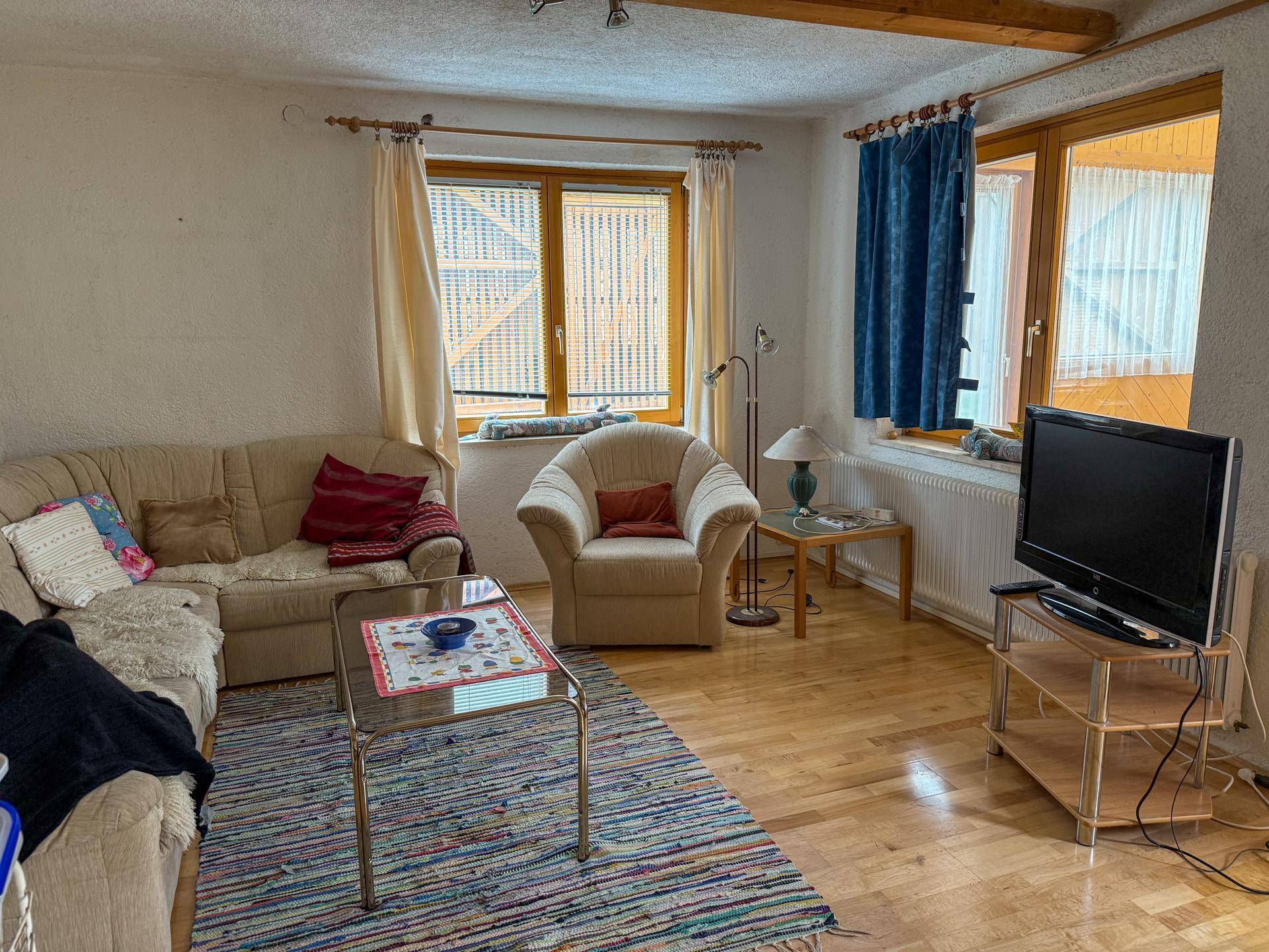 Gemütliches Wohnzimmer mit Holzboden, beigen Sofas und einem bunten Teppich.