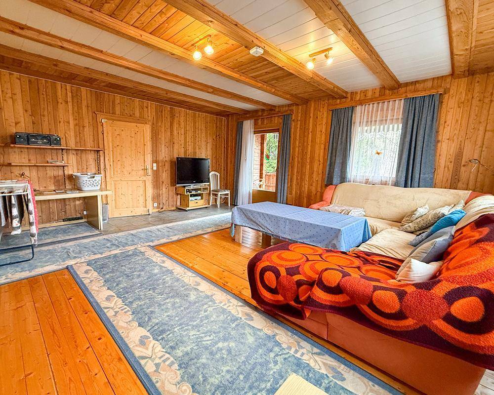 Rustikales Wohnzimmer mit Holzwänden, sichtbaren Deckenbalken und bequemen Sofas.