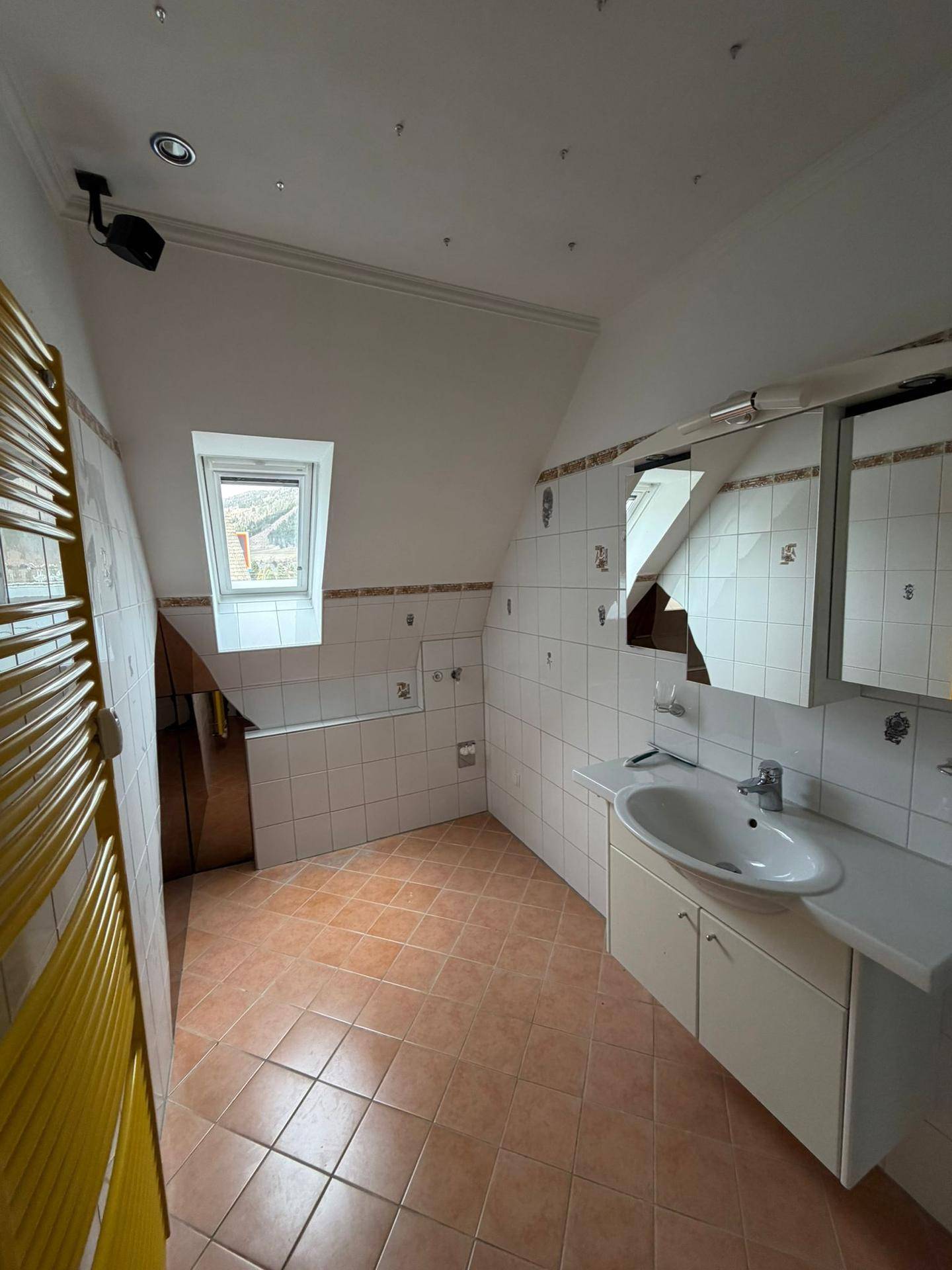 Badezimmer mit Dachschräge, Dachfenster, gelbem Handtuchheizkörper und terracottafarbenen Fliesen.