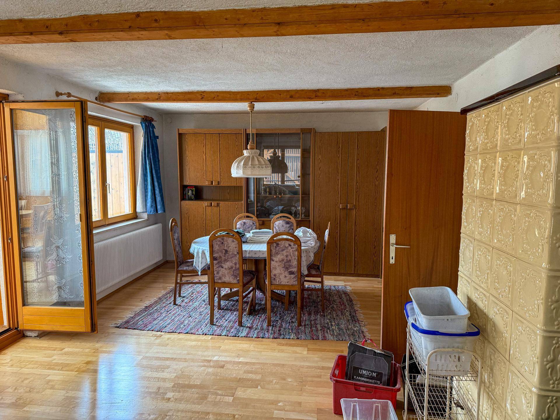 Essbereich mit Holztisch, Stühlen und einem traditionellen Kachelofen in der Ecke.